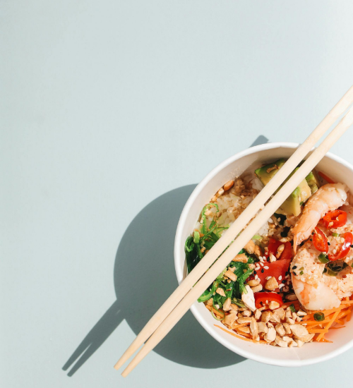 blue background with thai dish in a bowl with chopsticks laying diagnollly